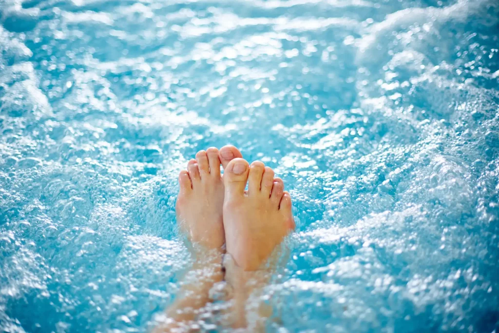 Close-up on someone's feet in the rolling water of a hot tub. A hydro massage in warm water is a good way to reduce joint pain in your spa.