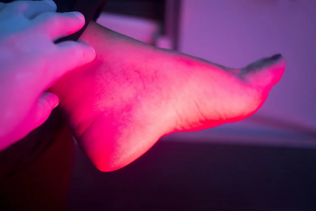 Close up of a foot under the glow of a red light therapy device. A sauna with red light therapy can accelerate numerous wellness and healing processes.