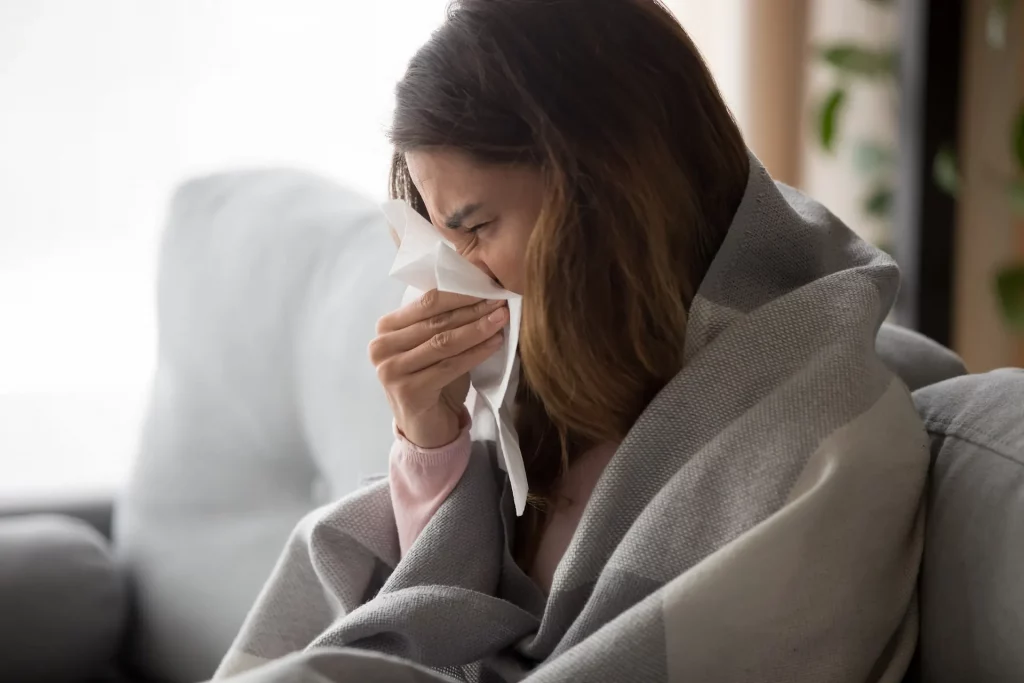A person blows their nose while wrapped in a blanket. Hot tubs are effective at helping combat cold symptoms like congestion and fatigue.