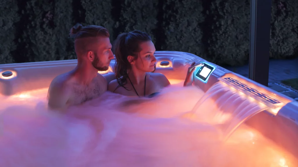 Two bathers sit close together in a Wellis hot tub with amber lighting for a romantic date night.