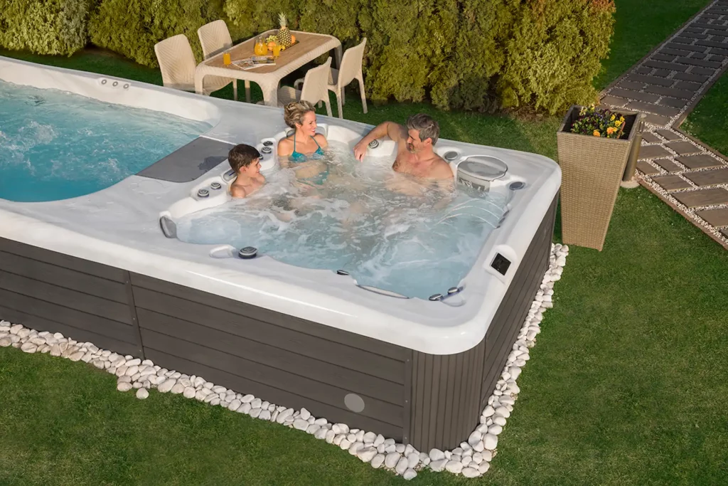 Two parents and a child sit in the hot tub section of a Wellis Swim Spa. The unique opportunity to spend time with family in the backyard is one reason why kids love swim spas.