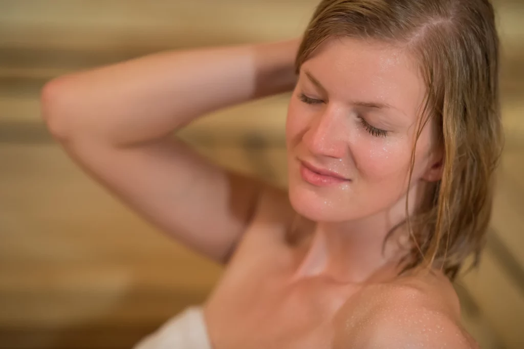 Close up on a person sitting in a sauna while wrapped in a towel. Schedule and lifestyle are important factors to consider when deciding the best time of day to use a sauna."
